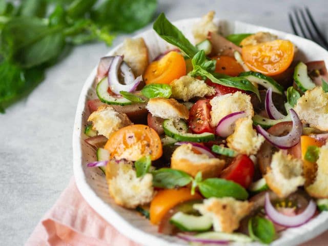Eine Schüssel mit italienischem Brotsalat und daneben eine Gabel und frisches Basilikum.
