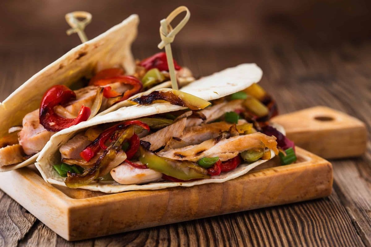 Weizen-Tortillas mit gegrilltem Hähnchenfleisch, Paprika und Zwiebeln auf einem Holz-Serviertablett