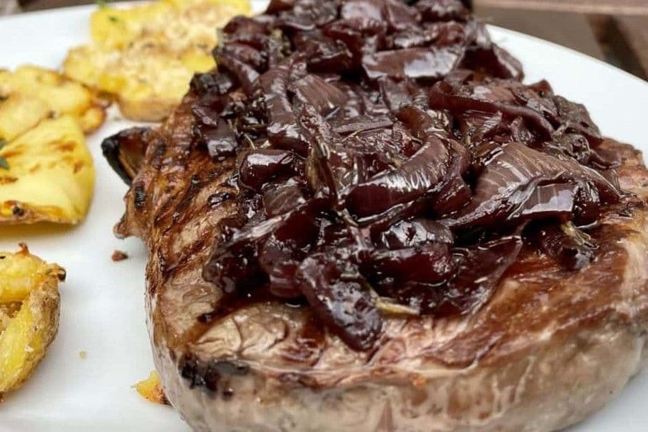 Gegrilltes Entrecote mit Rotwein-Zwiebeln und Quetschkartoffeln auf einem weißen Teller