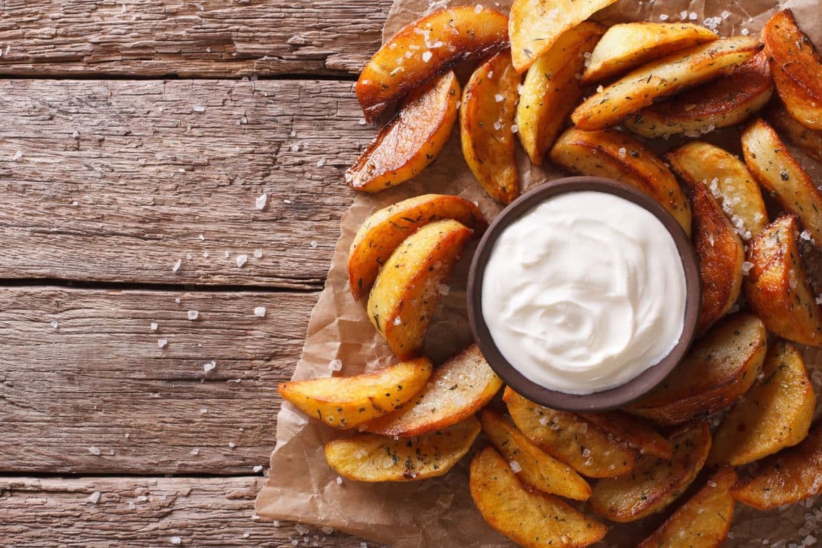 knusprige Kartoffel Wedges mit Sour Cream Dip auf Holzbrett