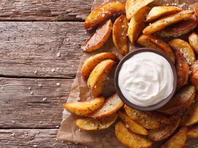 knusprige Kartoffel Wedges mit Sour Cream Dip auf Holzbrett