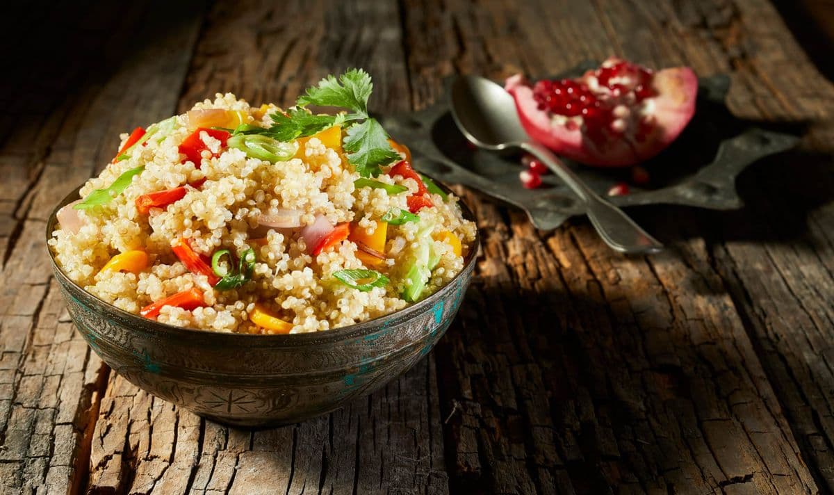 Hier liegt eine Schale mit Couscous Salat und im Hintergrund ein Granatapfel mit einem Löffel auf einem Teller.
