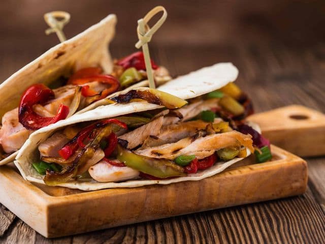 Weizen-Tortillas mit gegrilltem Hähnchenfleisch, Paprika und Zwiebeln auf einem Holz-Serviertablett