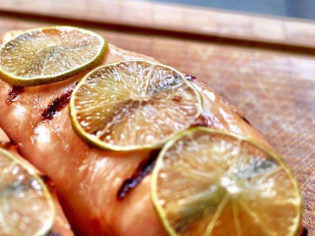 Gegrillte Hähnchenfilets mit Radler-Glasur und mitgegrillten Limettenscheiben auf einem Holzbrett