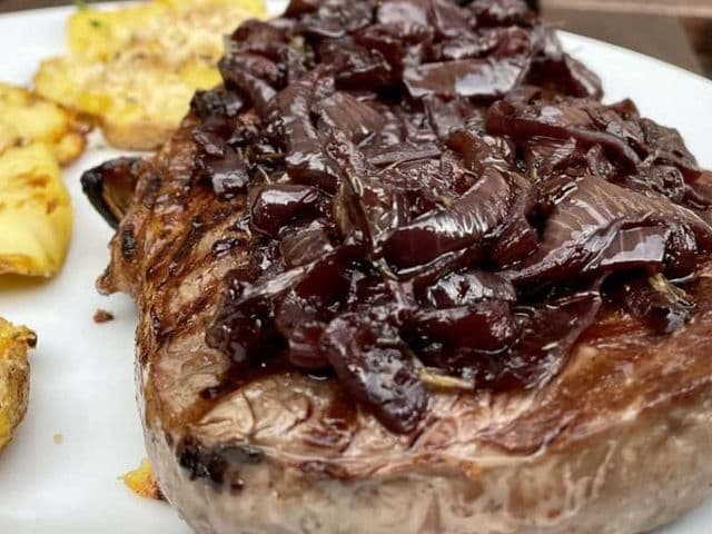Gegrilltes Entrecote mit Rotwein-Zwiebeln und Quetschkartoffeln auf einem weißen Teller