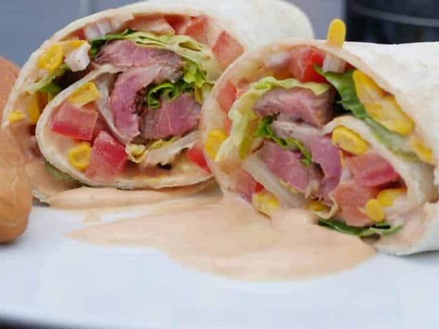 Angeschnittener Steak Burrito mit Entrecote-Streifen, Mais, Tomate und Salat, daneben Brötchen und Sauce