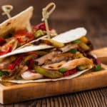 Weizen-Tortillas mit gegrilltem Hähnchenfleisch, Paprika und Zwiebeln auf einem Holz-Serviertablett